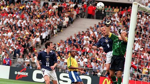  Scotland vs Brazil group match during the 1998 World Cup in France. Close-up shows three players and a goalie by the goal as a ball flies into the air. Behind them is the crowd in the stands watching in anticipation