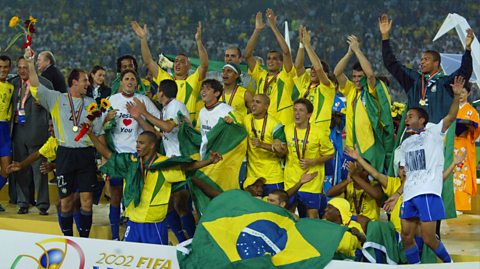 Brazil during their last victory in 2002. The team stands on a podium cheering, wearing their yellow and green football kit