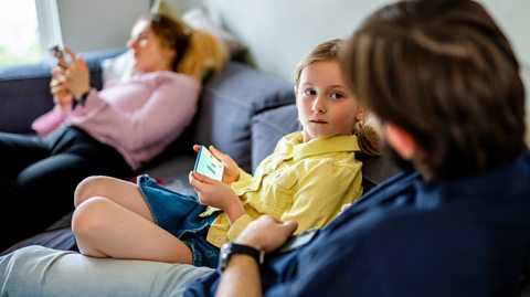 mum scrolls in background while daughter and dad talk about her phone use