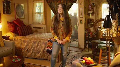 Ari Michelson/ AUGUST Loreen Willemberg, a woman with long hair, stands in the middle of a warmly lit, homely decorated sitting room (Credit: Ari Michelson/ AUGUST)