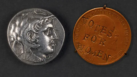 Alamy/ Getty Images An ancient Greek silver coin depicting a man wearing a lion-skin headdress, next to a British penny from 1903 that was defaced by suffragettes in the early 20th Century with the words "Votes for women" (Credit: Alamy/ Getty Images)