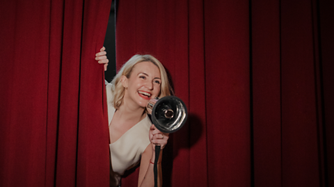 image of Charlotte Lewis, confidence coach, peering out of a red curtain, holding a megaphone