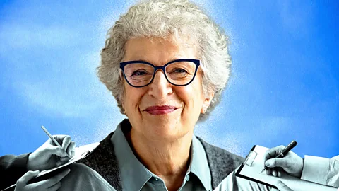 Serenity Strull/ BBC/ Getty Images An older woman with white hair and glasses smiles, while the hands of therapists writing notes surround her (Credit: Serenity Strull/ BBC/ Getty Images)
