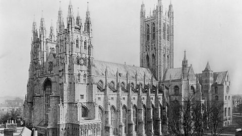 A landscape image of Canterbury Cathedral. It's a large medieval cathedral built in the Romanesque and Gothic styles, with a soaring central bell tower and asymmetrical twin towers at its western front.
