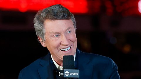 Wayne Gretzky, a white man in his sixties with short grey hair, speaks into a microphone as he commentates on a sports show.