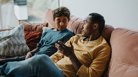 Father talking with son while sitting on sofa in living room at home