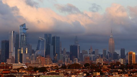 A landscape image shows the Manhattan skyline at sunset. The sky is a mix of purples, pale yellows and blues. The most prominent building visible is the huge Empire State Building.
