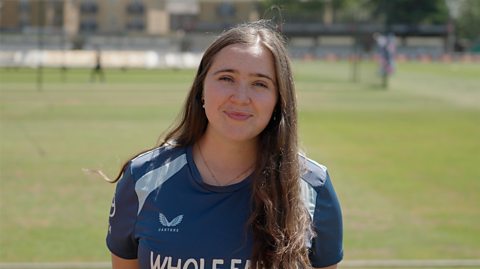 Emily Marshall, a digital content producer for England Women's cricket, on a sunny pitch.