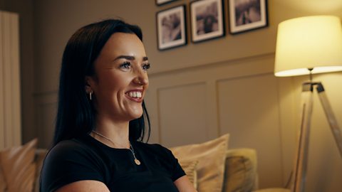 Yasmin smiles off-camera in her warmly lit living room.