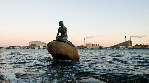 The Little Mermaid statue in Copenhagen, Denmark. The mermaid statue sits on a rock in the water.