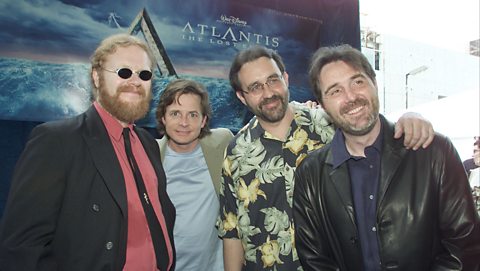 Co-directors Gary Trousdale (left) and Kirk Wise (right) with Michael J. Fox and producer Don Hawn at the world premiere of Atlantis: The Lost Empire. A poster advertising the film is behind them as they pose together on the red carpet