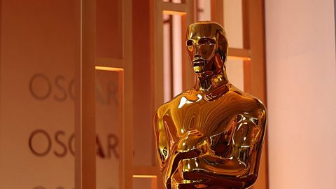 An image of the Oscar statuette that cuts off at the waist. It is a gold-coloured statue of a knight holding a sword, stood atop a film reel.