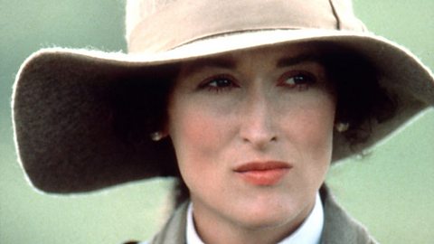A close-up colour photograph of actress Meryl Streep in the film 'Out of Africa'. She's wearing a wide-brimmed hat and looking seriously off to the right of the camera.