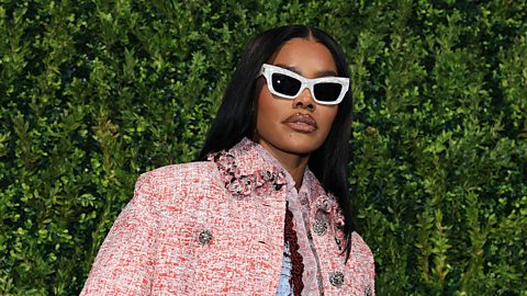 A photo of actress Teyana Taylor from a fashion shoot. She's wearing a large light brown fur-look jacket and large white sunglasses.