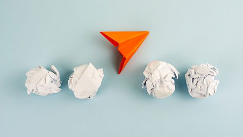 Scrunched up pieces of paper surround an orange arrow that's pointing upwards, suggesting onwards movement. 