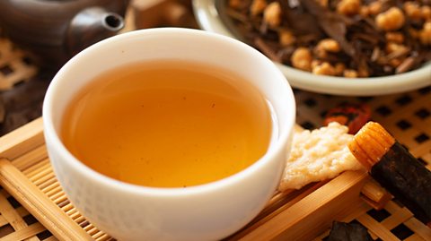 On a bamboo coaster is a white cup with no handles full of hojicha tea water (with the tea leaves removed). It is an orange colour