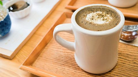 On a wooden table is a white mug containing a Hojicha Latte - made from hojicha tea leaves. It is brown in colour and frothy at the top