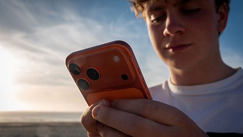 An image of a young boy looking at his phone during sunset