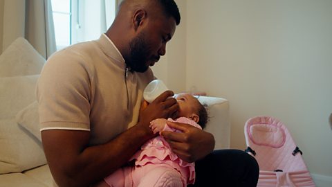 Man cradles baby whilst feeding her a bottle.