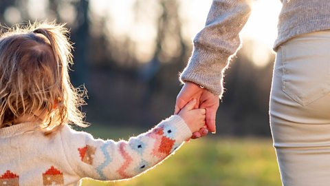 A child on the left holds the hand of a parent on the right; we only see the arm and leg of the parent.