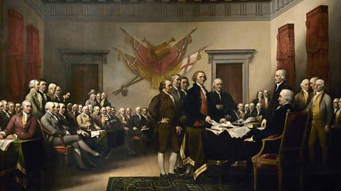 Painting showing Thomas Jefferson, John Adams, Roger Sherman, Robert Livingston, and Benjamin Franklin presenting the first draft of the Declaration of Independence to the Second Continental Congress. The room is filled with men wearing long tailed coats, vests, knee-length breeches and white ruffled shirts