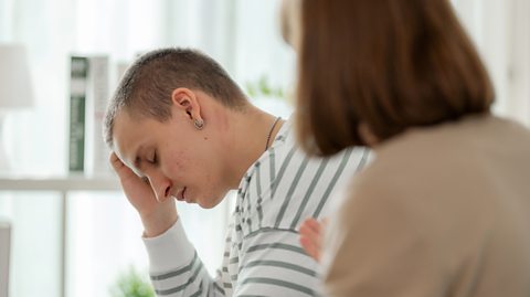 Depressed boy holds head in hands as mother attempts to comfort him