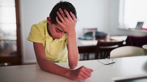 Boy is sad - sitting at a desk with his head in his hands