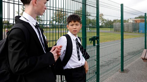 Two schoolboys in uniform at school fence - one looks to camera