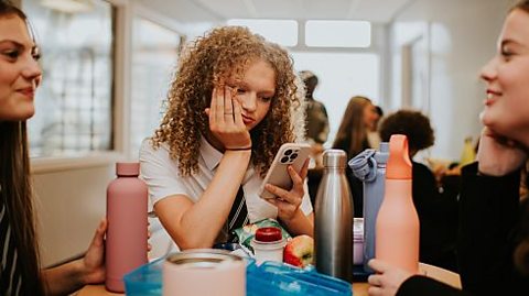Teenagers in the school canteen on mobile phones.