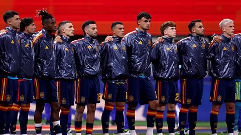 Spain players stand for the national anthem before the FIFA World Cup 2026 Group H match. Standing on the football pitch, they all have their arms around each others shoulders, wearing matching blue football kits