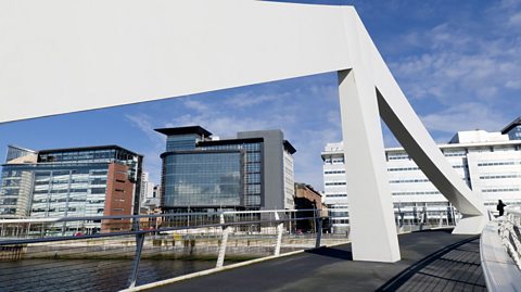Footbridge crosses River Clyde towards modern large glass multi-story buildings in the finance district in Glasgow