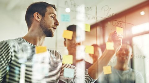 A man using Post-It notes to map out ideas, with colleagues in the background. 