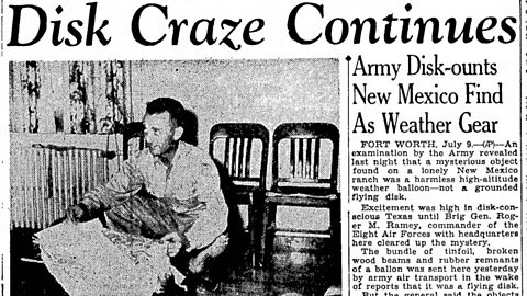 A newspaper article from the time of the Roswell Incident. The headline across the top reads 'Disk craze continues'. Underneath, a lede paragraph reads: 'Army disk-counts New Mexico find as weather gear'. To the left is an image of a military man holding a piece of the debris.
