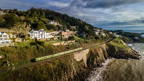 Getty Images A green Dart train travels along cliffs overlooking the Irish Sea with houses perched above the coastline (Credit: Getty Images)