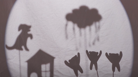 Shadow images in a shadow theatre - a dog and house on the left with a cloud and three teddy bears on the right.