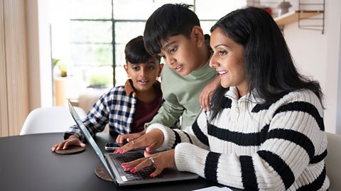 A mother and two young boys look at a laptop in a bright neat study for home education