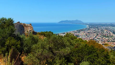 Alamy A jagged mountain promontory is at the end of a curving coastline, with Roman ruins in the foreground (Credit: Alamy)