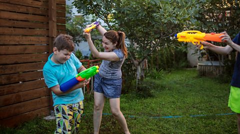 Brother and sister use water pistols and soakers to have summer fun in a garden