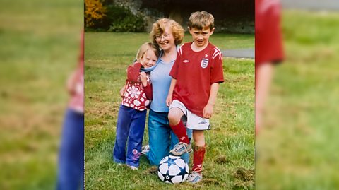 A young Elliot Jones, wearing an England football kit and with a ball at his feet, stands in a family photo