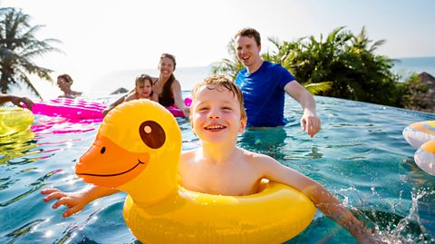 boy in yellow duck rubber ring with family behind him in a pool on holiday