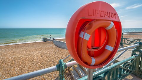 Lifebelt or lifebuoy in position on a promenade overlooking a pebbly beach and rough seas