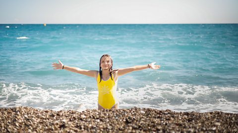 Girl in yellow swimming costume on pebbly beach