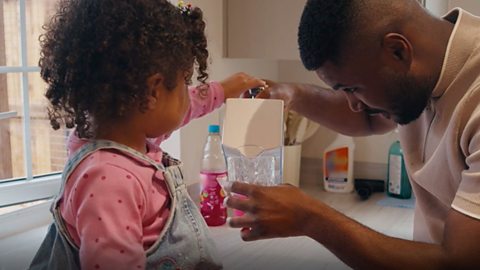Dad and daughter look at container as fruit drink about to be poured