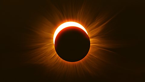 The image shows the night sky, cast in a dark red light. In the centre, the moon is almost completely eclipsing the sun. We can just see a crescent of the sun peaking out over the top of the moon.