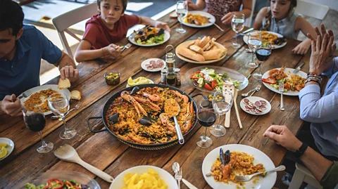 Getty Images A family sits around a table enjoying a large pan of seafood paella (Credit: Getty Images)