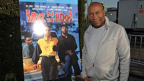 An image showing the director John Singleton alongside a poster from his 1991 film Boyz N the Hood 