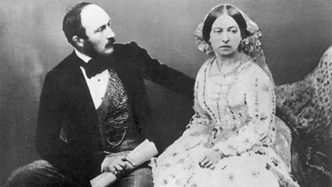 A black and white photograph of Queen Victoria and Prince Albert. They are sitting down next to each other, Albert on the left and Victoria on the right. Albert's head is turned to the side to look at his wife, while Victoria gazes off away from him with a serious expression. 