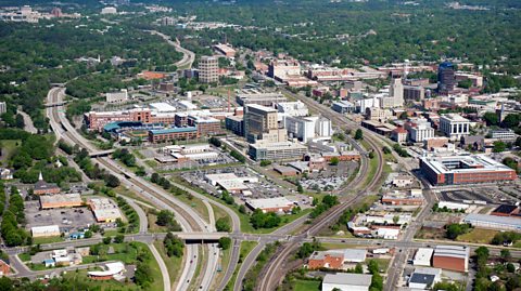 An aerial view of the downtown area of Durham, North Carolina in the day time, showing woodland in the distance and the city at the forefront 