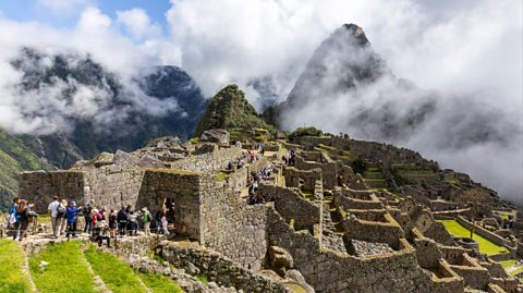 Tourists explore Machu Picchi, a historic citadel which consists of dry-stone walls and terraced fields, and is surrounded by cloud forests
