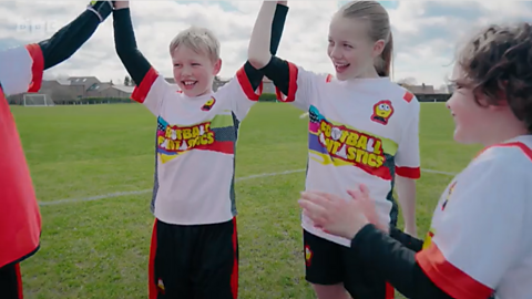 A group of four children on a football pitch, looking as if they are celebrating.